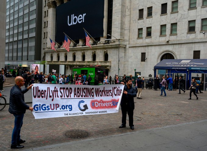 Two drivers hold up a protest sign as the Uber banner hangs on the front of the New York Stock Exchange May 10, 2019 in New York