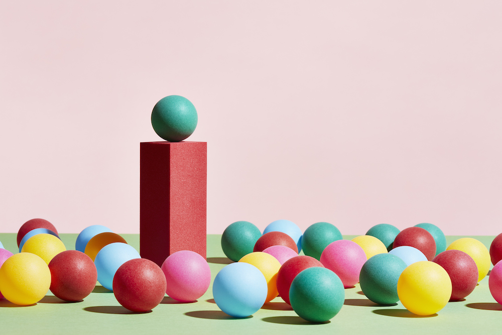 A green sphere stands on top of a pedestal surrounded by a crowd of multicoloured spheres