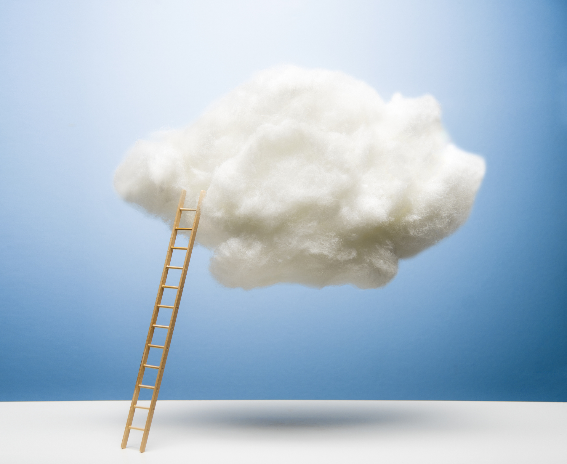 Ladder leaning on white puffy cloud on blue studio background, white surface, drop shadow